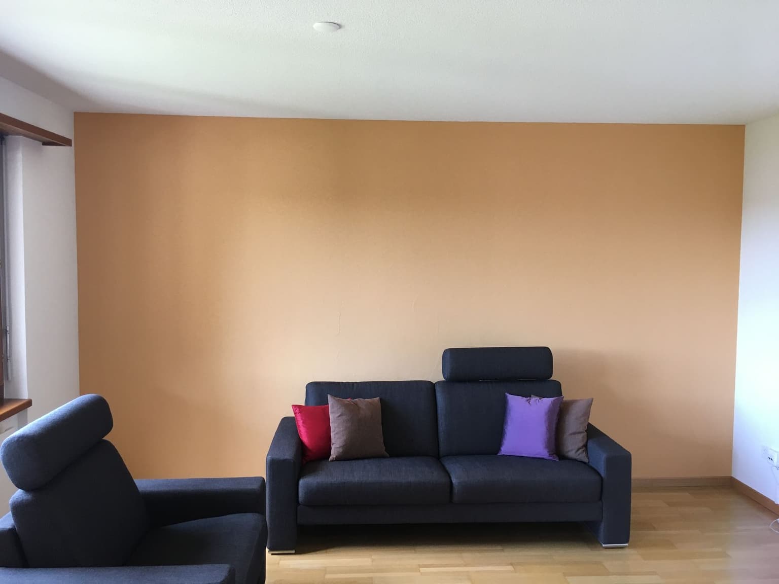 Wohnzimmer mit warm oranger Wandfläche und dunklem Sofa